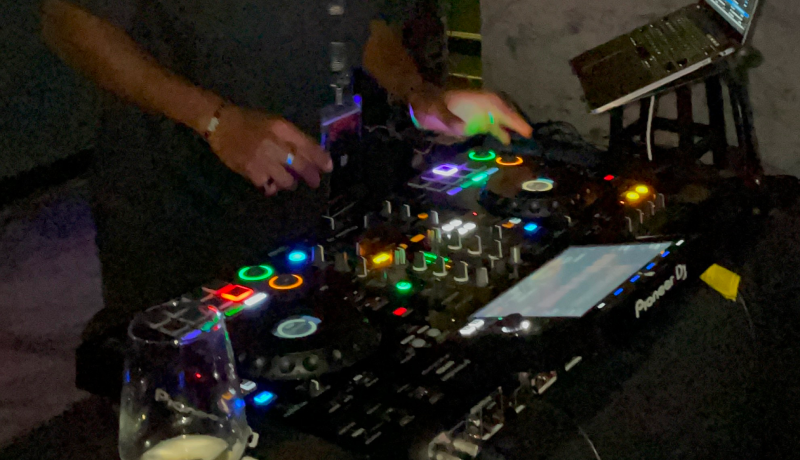 A DJ working a lit controller in a dark room, laptop open beside them